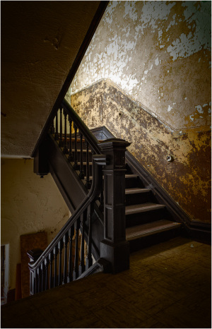 A charming old staircase with dark wooden railing and peeling paint on the walls.