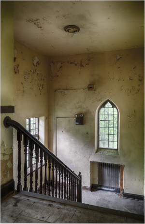 Interior view of a staircase with peeling walls and a gothic-style window.