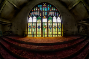 Stained glass windows with vibrant colors in an abandoned interior space.