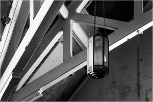 A vintage lantern hangs from a ceiling with wooden beams in black and white.