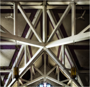 Intricate wooden beams form a surreal web above, contrasting light and shadow.
