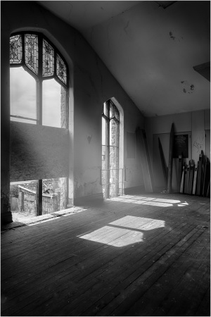 A spacious room with large windows, sunlight casting shadows on the floor.