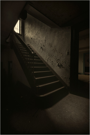 Dimly lit staircase with peeling walls and a window casting light