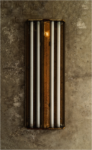 An industrial light fixture casting a warm glow on a rough concrete background.