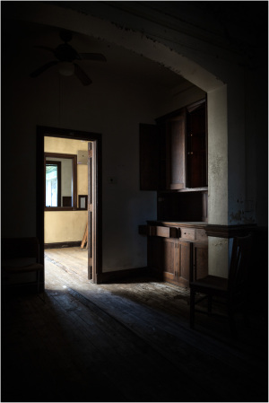 A dark room with a doorway leading to a brighter space, featuring wooden furniture.