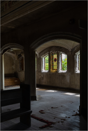 Interior space featuring arched windows and stained glass, with a dimly lit atmosphere.