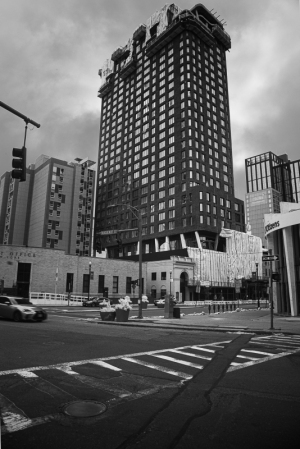 A tall building under construction in a city with a cloudy sky and street intersection.