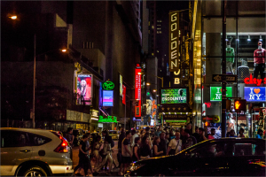 A busy street in New York City at night with bright neon signs and crowds of people.