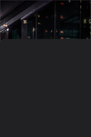 City lights reflected in a glass building at night, with people walking by.
