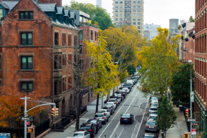 View of a city street lined with parked cars and trees in autumn colors.