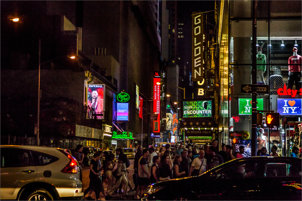 A busy street in New York City at night with bright neon signs and crowds of people.