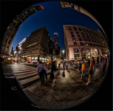 A busy New York City street at night with pedestrians and buildings under streetlights.