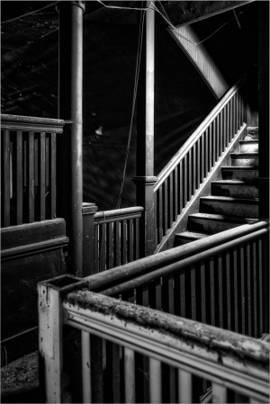 Weathered wooden staircase leading to an unknown upper floor, shadowed and enigmatic.