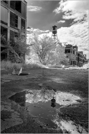 A desolate urban landscape with a puddle reflecting a watchtower and abandoned buildings.