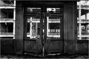 An old, weathered door stands ajar in a decaying building, shadows loom.