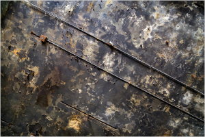 Rusty metal surface with streaks and bolts, showcasing weathered textures.