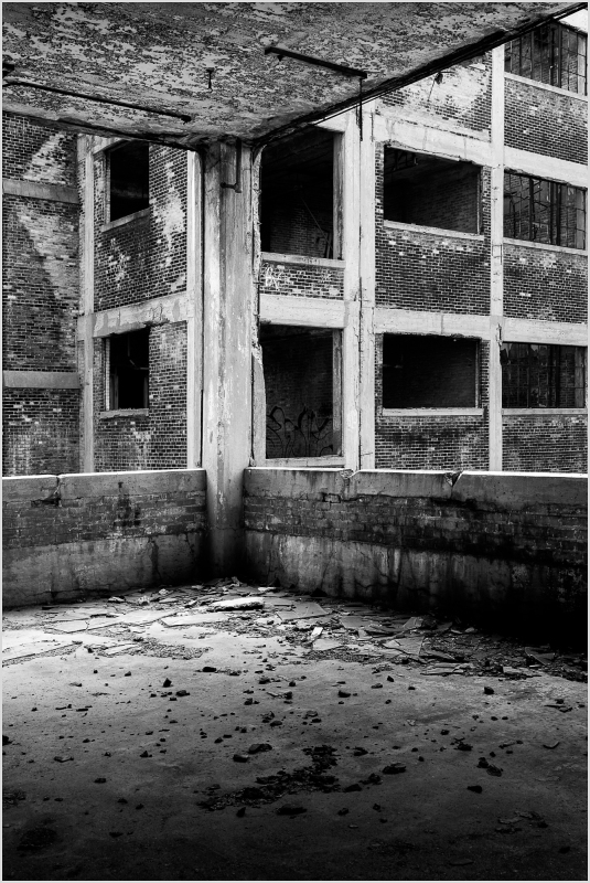 Abandoned interior with crumbling walls and empty window frames, shadows loom.