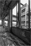 Interior view of a dilapidated building with broken windows and debris on the floor.