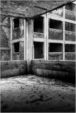 Abandoned interior with crumbling walls and empty window frames, shadows loom.
