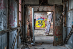 A view through broken doors revealing colorful graffiti on a wall in an abandoned building.