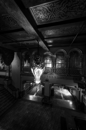 A grand chandelier hangs in a dimly lit theater, shadows dance on ornate walls.