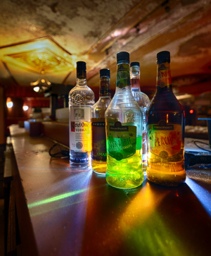A collection of illuminated bottles on a bar, casting colorful reflections in the dim light.