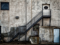 A weathered building with a metal staircase leading to a round door.