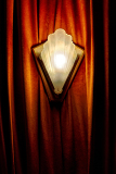 A vintage light fixture casts a soft glow against rich, draped fabric.