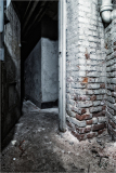 A narrow, dimly lit corridor with exposed brick walls and concrete floor.