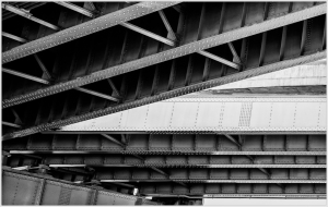 Underside view of a bridge with metal beams and supports in black and white.