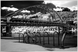 A black and white image of a bridge over a river with a bicycle parked nearby.