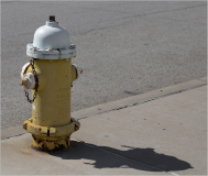 A yellow fire hydrant with a white top and chain on a sidewalk.