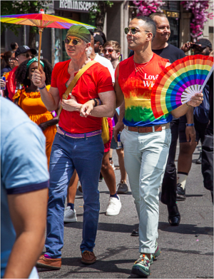 Two men in colorful outfits parade with rainbow accessories during a pride event.
