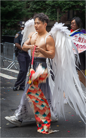 A person with angel wings walks in a parade, embodying vibrant pride and celebration.