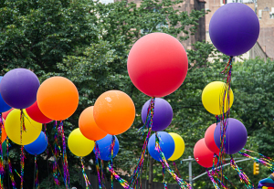 Colorful balloons in red, orange, yellow, and purple float above green trees.