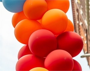 A vibrant tower of red, orange, and blue balloons against a soft sky.