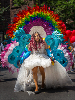 A vibrant figure adorned in a white gown and colorful feathers strides confidently through a festive scene.