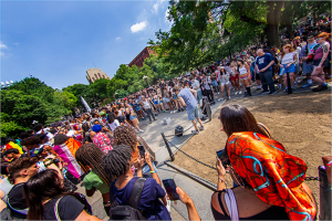 A vibrant crowd gathers in a park, captivated by a performer amidst lush greenery.