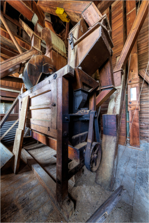 A weathered wooden mill machine sits in a dimly lit, rustic interior filled with shadows.