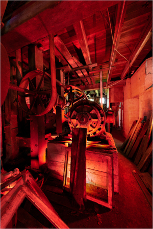 Gloomy interior of an old mill with ominous red lighting and vintage machinery.