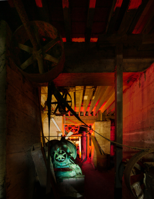Gears and machinery bathed in a surreal glow, shadows loom in an industrial haunt.