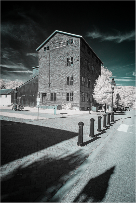 A historical mill building with wooden exterior and multiple windows, captured in infrared.
