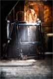 Old black metal frame rests against weathered wooden walls, light softly illuminates dust.