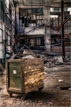 An old, weathered cart in an abandoned industrial space with debris and broken windows.