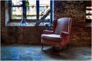 An abandoned armchair sits in a desolate space, its fabric weary and worn.