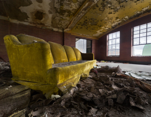 A worn yellow couch rests amid decaying remnants of an abandoned space.