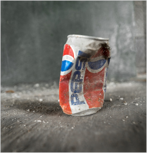 A crumpled can rests upon a silent, dusty floor, time's passage etched in its battered form.