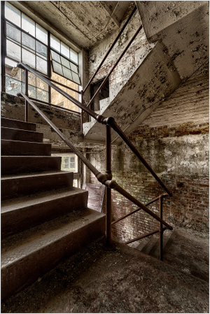 Weathered stairs ascend through quiet decay, where silence clings to stone walls.