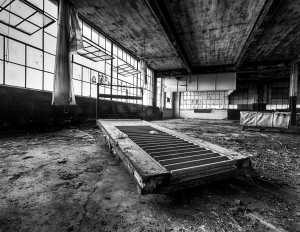 An abandoned interior with a long wooden platform and large windows letting in light.