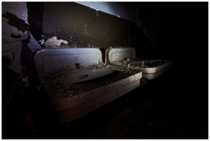Abandoned sinks shrouded in dust, a ghastly reminder of forgotten lives.